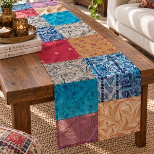 Könnte beinhalten: Ein rechteckiger Tischläufer mit einem Patchwork-Design aus verschiedenen Stoffquadraten in Blau-, Rot-, Gold- und Cremetönen. Die Stoffquadrate zeigen unterschiedliche Muster, darunter florale, Paisley- und botanische Drucke, die zusammengenäht sind.