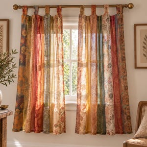 May include: A pair of tab-top curtains featuring vertical panels of varying patterns and colors, including shades of orange, red, yellow, green, and cream. The fabric is semi-sheer, allowing light to pass through, and hangs from a brass rod.