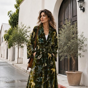 May include: A long-sleeved, calf-length olive green velvet robe featuring a repeating pattern of yellow leopards, white swans, and green palm leaves. The garment includes a matching fabric tie belt at the waist, two side pockets, and a shawl collar.
