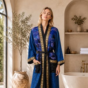 May include: A long-sleeved blue robe featuring a dark blue and purple abstract pattern, black trim, and gold-toned circular embellishments along the front opening, cuffs, and pockets. The robe includes a matching black tie belt at the waist.