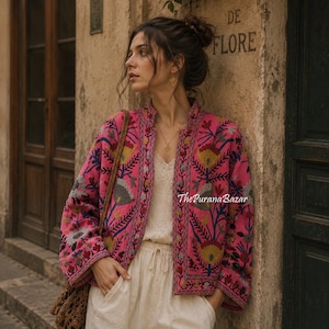 May include: A vibrant pink jacket featuring intricate multi-coloured floral embroidery in shades of yellow, blue, and grey. The jacket has a high collar, long sleeves, and an open front design. The text ThePuranaBazar is visible on the fabric.