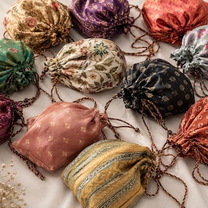 Può includere: Una collezione di dieci piccole borse con coulisse realizzate in vari tessuti fantasia, inclusi motivi floreali, geometrici e paisley in colori come oro, viola, rosso, verde, nero e blu, ciascuna dotata di cordini intrecciati abbinati.