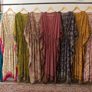 Puede incluir: Una colección de ocho vestidos caftán largos hasta el suelo colgados en un perchero, con varios patrones y colores que incluyen verde azulado, crema, amarillo mostaza, marrón, rojo oscuro, azul marino y estampados florales.