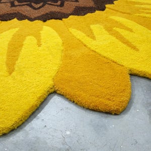 IN-108 Hand Tufted Sunflower Woolen Carpet for Floor Decor, Cozy Home,Bedroom, Courtyard, Living Room, Kids, Cabin, Bedroom, Reading Nook.
A vibrant sunflower-shaped wool rug handcrafted in rich yellow and brown tones, featuring realistic petal textures and a plush wool surface. Displayed in a bright minimalist room with indoor plants, natural sunlight, and a wooden bench, this handmade rug adds a cheerful botanical touch and cozy warmth to any modern living space.