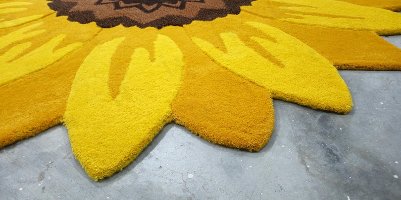 IN-108 Hand Tufted Sunflower Woolen Carpet for Floor Decor, Cozy Home,Bedroom, Courtyard, Living Room, Kids, Cabin, Bedroom, Reading Nook.
A vibrant sunflower-shaped wool rug handcrafted in rich yellow and brown tones, featuring realistic petal textures and a plush wool surface. Displayed in a bright minimalist room with indoor plants, natural sunlight, and a wooden bench, this handmade rug adds a cheerful botanical touch and cozy warmth to any modern living space.