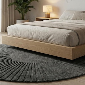 Könnte beinhalten: Ein modernes Schlafzimmer mit einem niedrigen Holzbett und neutraler Bettwäsche. Ein runder, dunkelgrauer Teppich mit radialem Muster liegt unter dem Bett. Eine Topfpflanze und eine Nachttischlampe ergänzen die Raumdekoration.