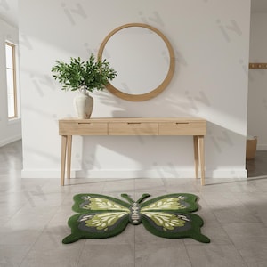 May include: A green and white butterfly-shaped rug on a tiled floor. The rug is in front of a light wood console table with a round mirror above it. A vase with greenery sits on the table. The rug's wings have a detailed design.