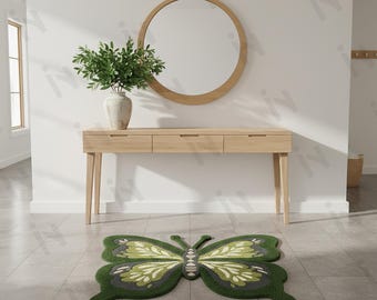 Puede incluir: Una alfombra con forma de mariposa verde y blanca sobre un suelo embaldosado. La alfombra está frente a una consola de madera clara con un espejo redondo encima. Un jarrón con vegetación está sobre la mesa. Las alas de la alfombra tienen un diseño detallado.
