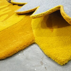 IN-108 Hand Tufted Sunflower Woolen Carpet for Floor Decor, Cozy Home,Bedroom, Courtyard, Living Room, Kids, Cabin, Bedroom, Reading Nook.
A vibrant sunflower-shaped wool rug handcrafted in rich yellow and brown tones, featuring realistic petal textures and a plush wool surface. Displayed in a bright minimalist room with indoor plants, natural sunlight, and a wooden bench, this handmade rug adds a cheerful botanical touch and cozy warmth to any modern living space.