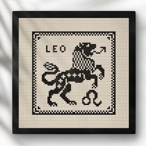 Puede incluir: Obra de arte en punto de cruz enmarcada con el signo zodiacal Leo. El diseño en blanco y negro representa un león con la palabra "LEO" encima. La obra está enmarcada en un marco negro.