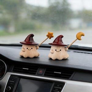 May include: Two wooden mushroom figurines with smiling faces, wearing burgundy witch hats. One holds a star wand, the other a crescent moon wand. The figurines are light brown with dark brown hats and wands.