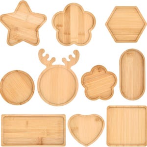 May include: A collection of ten light brown bamboo wooden trays in various shapes including a star, a hexagon, a heart, a rectangle, a square, an oval, two flowers, a circle, and a circular tray featuring decorative reindeer antlers.