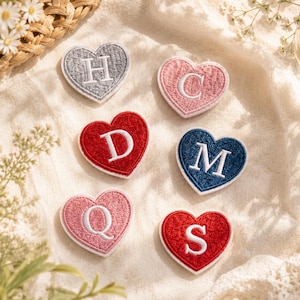 May include: Six heart-shaped embroidered patches featuring the letters H, C, D, M, Q, and S. The patches are rendered in various colors including grey, light pink, red, and dark blue, each with a white border and a white embroidered letter.
