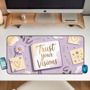 Puede incluir: Alfombrilla de escritorio rectangular con fondo lavanda que presenta un cuaderno con el texto "Trust your Visions". La alfombrilla incluye ilustraciones florales y de corazones, clips y un smartphone.