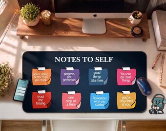 May include: A black desk mat with the text "NOTES TO SELF" and motivational quotes. The mat features colorful sticky notes with phrases like "You're doing better than you think" and "You can do Hard Things". A smartphone, mouse, and other desk items are also visible.