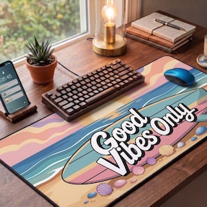 May include: A desk setup featuring a "Good Vibes Only" mousepad with a surfboard design. A wooden keyboard, blue mouse, and smartphone on a stand are also present. A small succulent in a pot and a drink are visible.