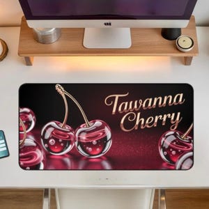 Puede incluir: Alfombrilla de escritorio negra con un diseño de cerezas brillantes y el texto "Tawanna Cherry" en escritura dorada. La alfombrilla está sobre un escritorio blanco con un monitor de computadora y una vela encendida.