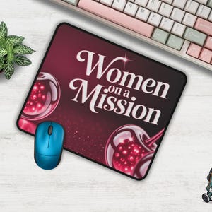 Puede incluir: Alfombrilla de ratón rectangular con el texto "Women on a Mission" en escritura blanca sobre un fondo rojo oscuro. El diseño incluye dos imágenes estilizadas de cerezas. También se ven un ratón azul y un teclado.