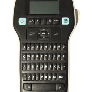 May include: A black and white DYMO label maker with a QWERTY keyboard, number keys, and function buttons. The device has a small screen and the brand name "DYMO" is printed on the top. The label maker is designed for creating custom labels.