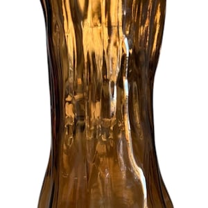 Può includere: Un vaso di vetro marrone con un design unico e strutturato. Il vaso ha una base ampia e svasata e una parte superiore più stretta, con un'altezza di circa 20 cm. La superficie ha un effetto increspato, creando interesse visivo. Ideale per l'arredamento della casa.