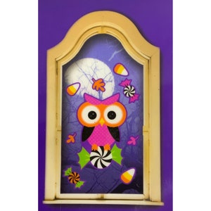 Puede incluir: Un b&uacute;ho rosa con ojos naranjas y alas negras se sienta sobre un caramelo en espiral. El b&uacute;ho est&aacute; rodeado de ma&iacute;z dulce, hojas y caramelos en espiral. La imagen est&aacute; sobre un fondo morado con una luna y &aacute;rboles.