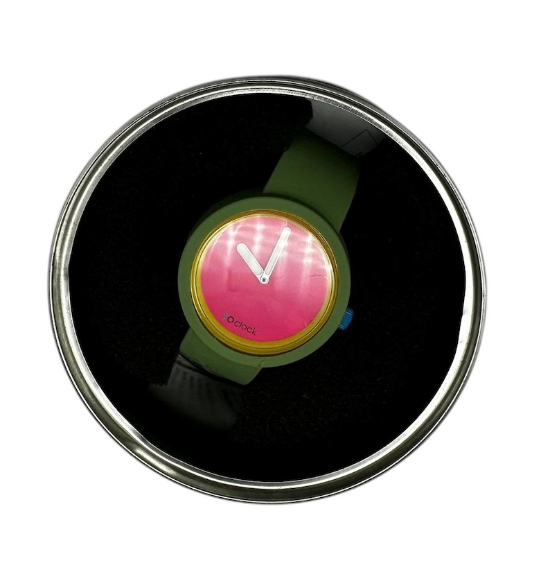 Pu&ograve; includere: Un orologio da polso verde con un quadrante rosa e un bordo dorato. L'orologio ha un quadrante bianco con lancette nere e la parola "o'clock" stampata sul quadrante.