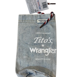 May include: A light blue denim bottle bag featuring a red, white, and blue drawstring cord. The front is printed with the text American Spirit, Tito's, Wrangler, and Quality Goods. A product tag is attached to the top with a barcode and text.