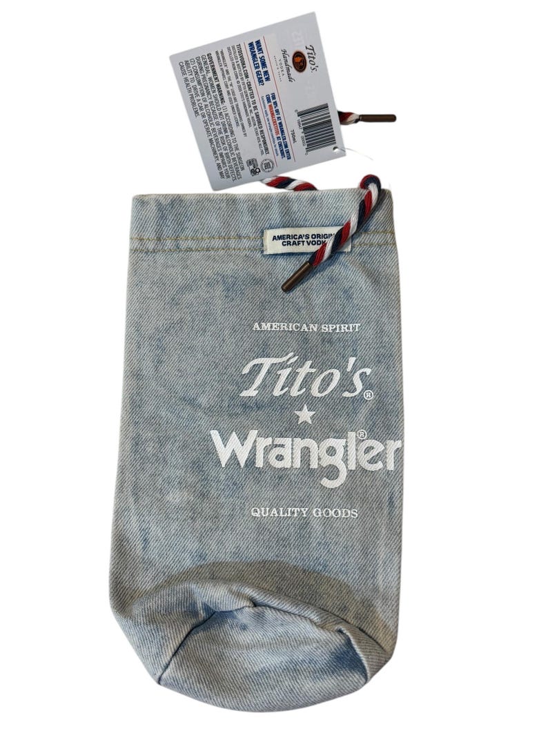May include: A light blue denim bottle bag featuring a red, white, and blue drawstring cord. The front is printed with the text American Spirit, Tito's, Wrangler, and Quality Goods. A product tag is attached to the top with a barcode and text.