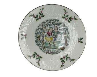 May include: White ceramic Christmas plate with a gold rim. The plate features a winter scene with two children ice skating. The scene is surrounded by holly sprigs. The text "Christmas 1972" is printed at the bottom of the plate.