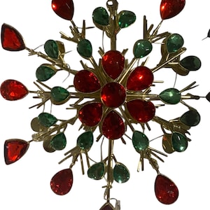 May include: A gold-coloured metal snowflake ornament, decorated with red and green teardrop-shaped jewels. This festive holiday decoration is designed to be hung. The ornament's design is reminiscent of a snowflake.
