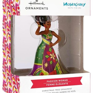 Peut inclure: Ornement de Noël Hallmark avec une figurine de femme élégante. La figurine porte une robe colorée avec des motifs verts, violets et jaunes. La boîte indique "Mahogany" et "Femme Élégante".