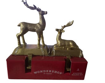 May include: A gold-colored metal stocking holder set featuring two reindeer figures. One reindeer stands, the other reclines. The set is on a red box with the text "Wondershop at Target" and "Stocking Holder Set".