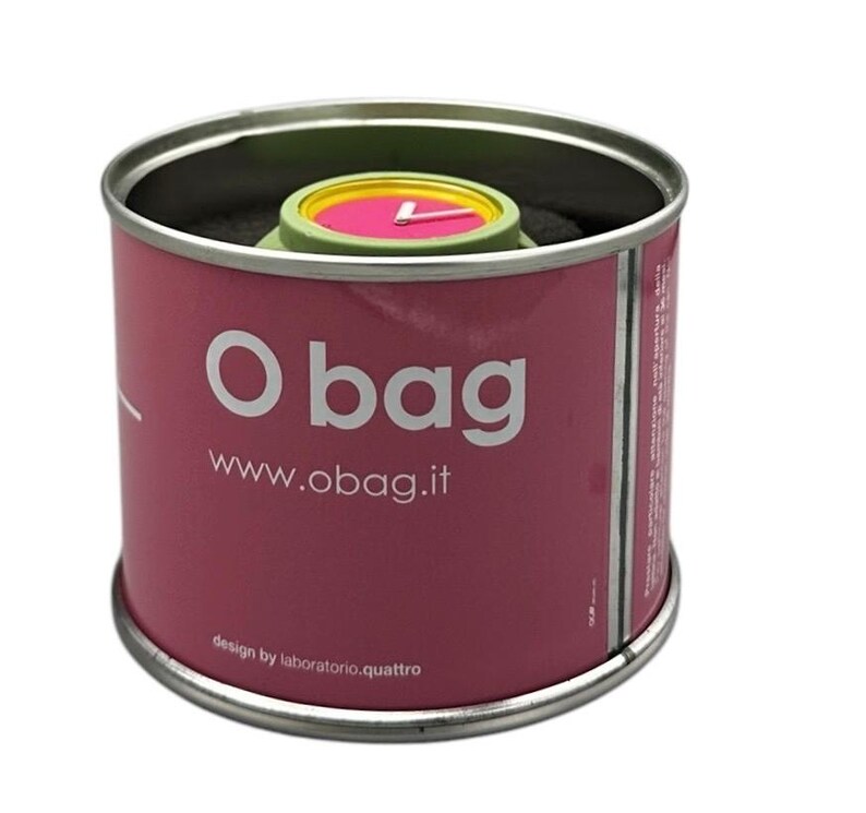Pu&ograve; includere: Un orologio da polso rosa e verde con una lancetta dei secondi gialla in un contenitore cilindrico di latta rosa e bianco con il testo "O bag" e "www.obag.it" sul lato. Il testo "design by laboratorio.quattro" &egrave; stampato sul fondo del contenitore.
