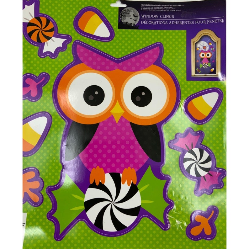 Puede incluir: Un conjunto de pegatinas de ventana reutilizables para Halloween con un b&uacute;ho rosa y naranja con ojos grandes, sosteniendo un bast&oacute;n de caramelo. El conjunto tambi&eacute;n incluye ma&iacute;z dulce, bastones de caramelo y hojas. El texto "Window Clings Decorations Adherentes Pour Fenetre" est&aacute; impreso en el embalaje.