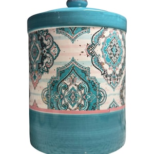 Puede incluir: Un tarro de cerámica turquesa con tapa. El tarro presenta un patrón decorativo de diseños florales turquesa y rosa sobre un fondo blanco. La base y la tapa son de color turquesa liso.