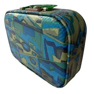May include: Vintage suitcase with a geometric pattern in shades of blue, green, and gray. The small suitcase has a rounded shape, a metal clasp, and a green handle. The exterior features a repeating abstract design.