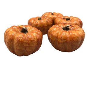 May include: Four small, orange, pumpkin-shaped candles. The candles have a slightly textured surface and a small, dark brown stem on top.