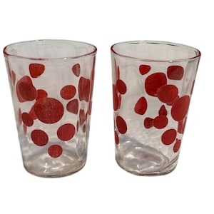 Peut inclure: Deux verres à boire transparents avec un motif de pois rouges. Les verres sont cylindriques avec un dessus légèrement évasé. Les points rouges varient en taille et sont répartis sur la surface du verre.