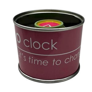 Pu&ograve; includere: Una scatola cilindrica rosa con un coperchio argentato. La scatola ha il testo "O clock it's time to change" stampato su di essa. All'interno della scatola c'&egrave; un orologio verde e rosa.
