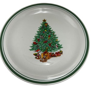 Peut inclure: Une assiette en céramique blanche avec un bord vert présente un motif d'arbre de Noël. L'arbre est décoré de boules, de cannes en sucre et de cadeaux. Un ours en peluche est assis au pied de l'arbre.