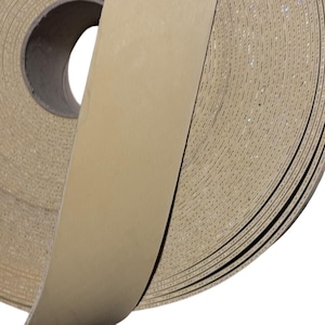 May include: A large roll of light tan, textured adhesive tape featuring a smooth, solid-colored strip extending from the center. The tape has a visible, fine-grained surface pattern throughout the coiled layers and a dark circular core.