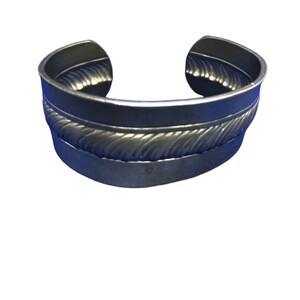 May include: A silver metal cuff bracelet with a rope-like design around the centre.