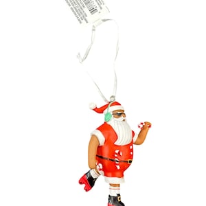 Peut inclure: Une décoration de Noël rouge et blanche représentant le Père Noël portant un casque et des patins à roulettes. Il tient une canne en sucre dans chaque main. La décoration est munie d'une ficelle blanche pour l'accrocher.