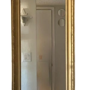 May include: A rectangular wall mirror featuring a metallic gold frame with a decorative, textured border pattern. The mirror has a smooth, reflective glass surface that displays a clear reflection of the surrounding interior space.