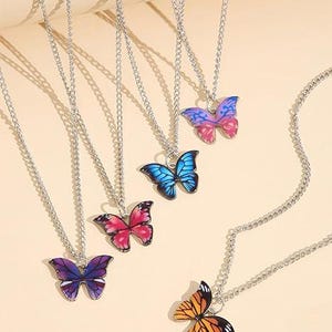 May include: A collection of silver-toned necklaces, each featuring a colorful butterfly pendant. The butterfly pendants are in various colors, including purple, blue, pink, and orange. The necklaces are displayed on a light beige surface.