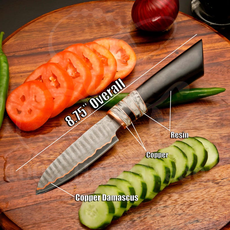 May include: A handcrafted knife with an overall length of 8.75 inches. The blade features a copper damascus design, and the handle is made of resin and copper. Sliced tomatoes and cucumbers are arranged on a wooden cutting board.