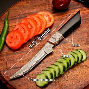 May include: A 9.75-inch overall Damascus steel knife with a black resin handle and copper accents. The knife is shown with sliced tomatoes and cucumbers on a wooden cutting board. The blade has a unique pattern.