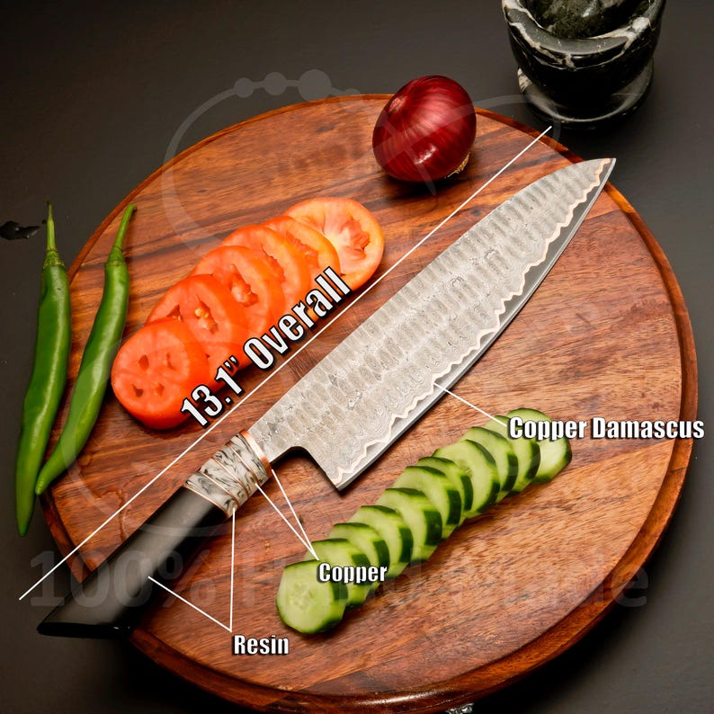 May include: A 13.1-inch overall copper Damascus chef's knife with a black resin handle, resting on a wooden cutting board. Sliced tomatoes, cucumbers, a red onion, and green chili peppers are also on the board.