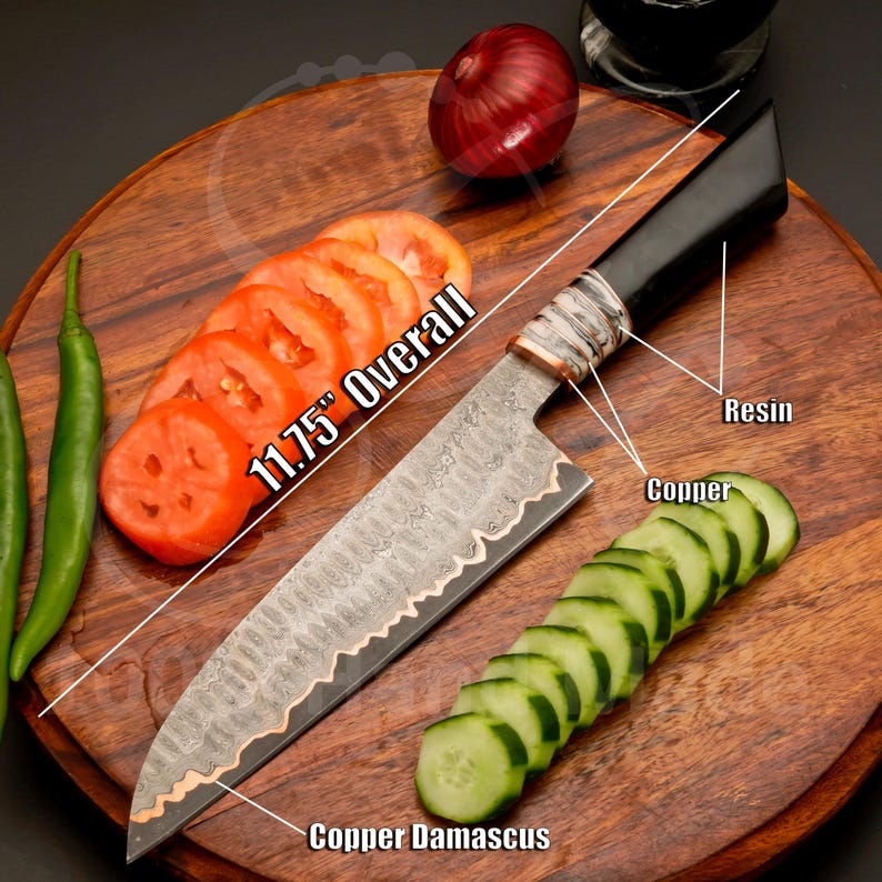 May include: A Damascus steel chef's knife with a black resin handle and copper accents. The knife is 11.75 inches overall and is shown with sliced tomatoes and cucumbers on a wooden cutting board. The blade has a copper edge.