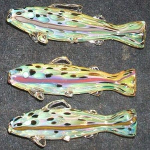 May include: Three glass fish figurines. Each fish is a different color, with a mix of green, yellow, and blue. The fish have black spots and clear fins. The fish are arranged in a row.